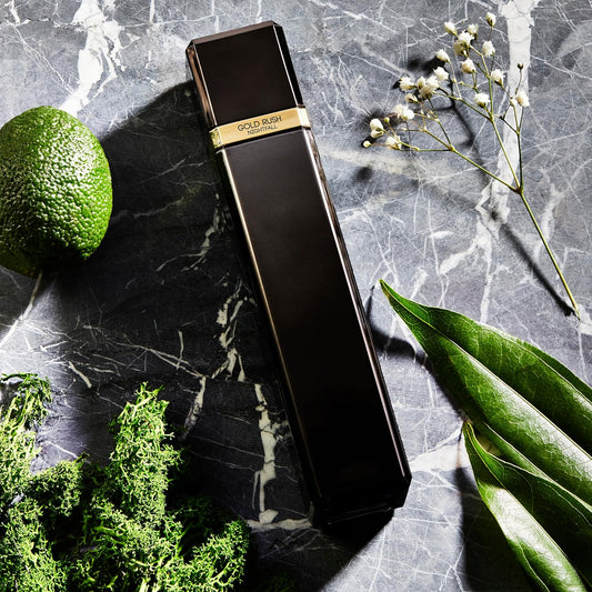 Black and gold perfume bottle on a marble surface with green leaves and flowers.