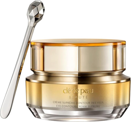 A gold and clear cosmetic cream jar with a faceted silver applicator spoon, shown on a clean white background. The brand name 'clé de peau BEAUTE' is visible on the front of the jar.