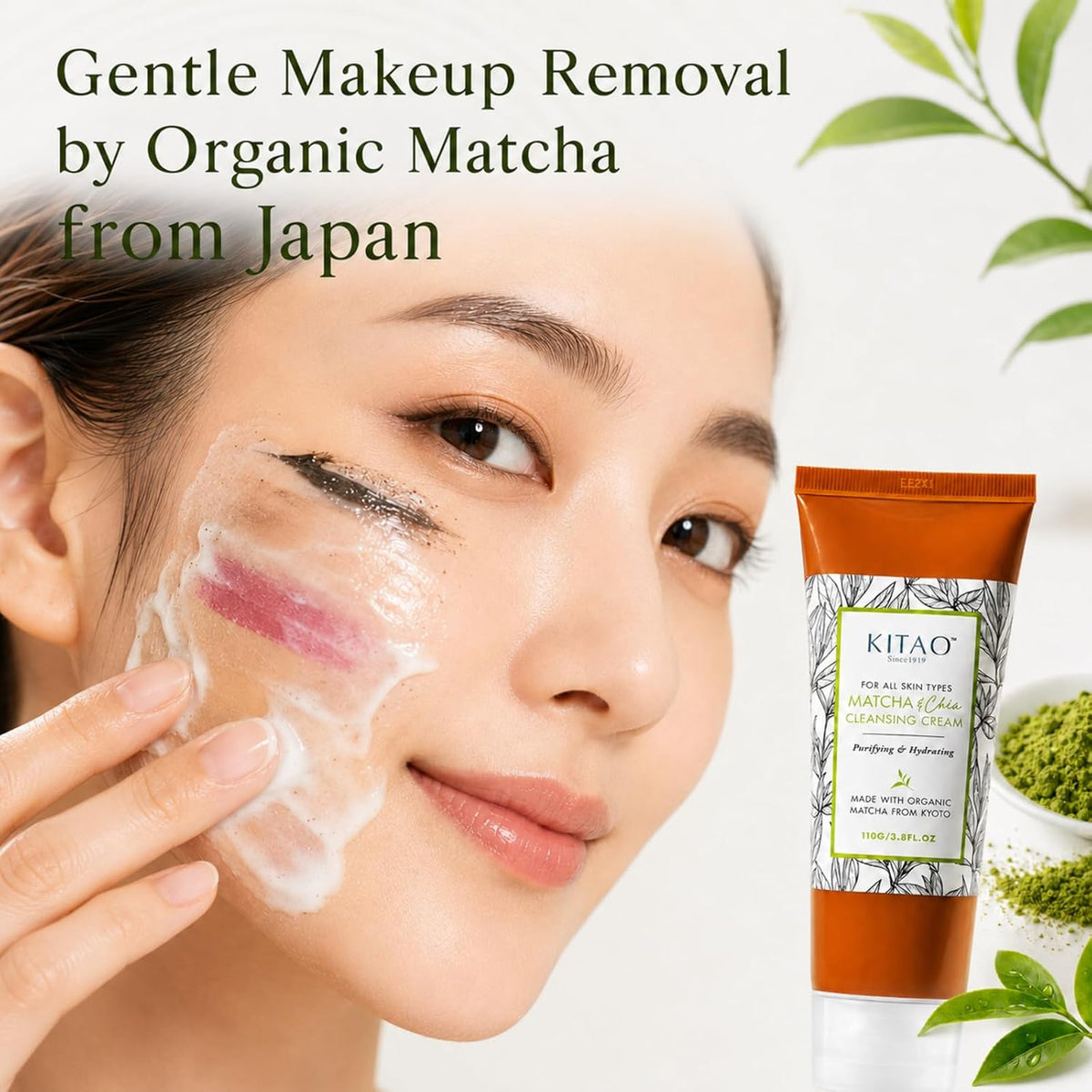 A woman applies a white makeup-removal cream to her cheek while the image advertises KITAO Organic Matcha Cleansing Cream. The product packaging is an orange squeeze tube with a white and green label, shown next to a small bowl of green matcha powder and decorative leaves on a clean white background.