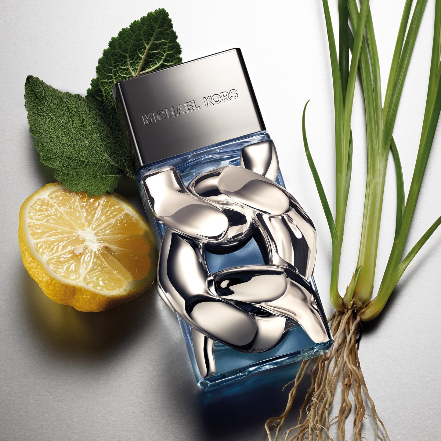 Blue Michael Kors perfume bottle with a lemon and plant on a light gray background