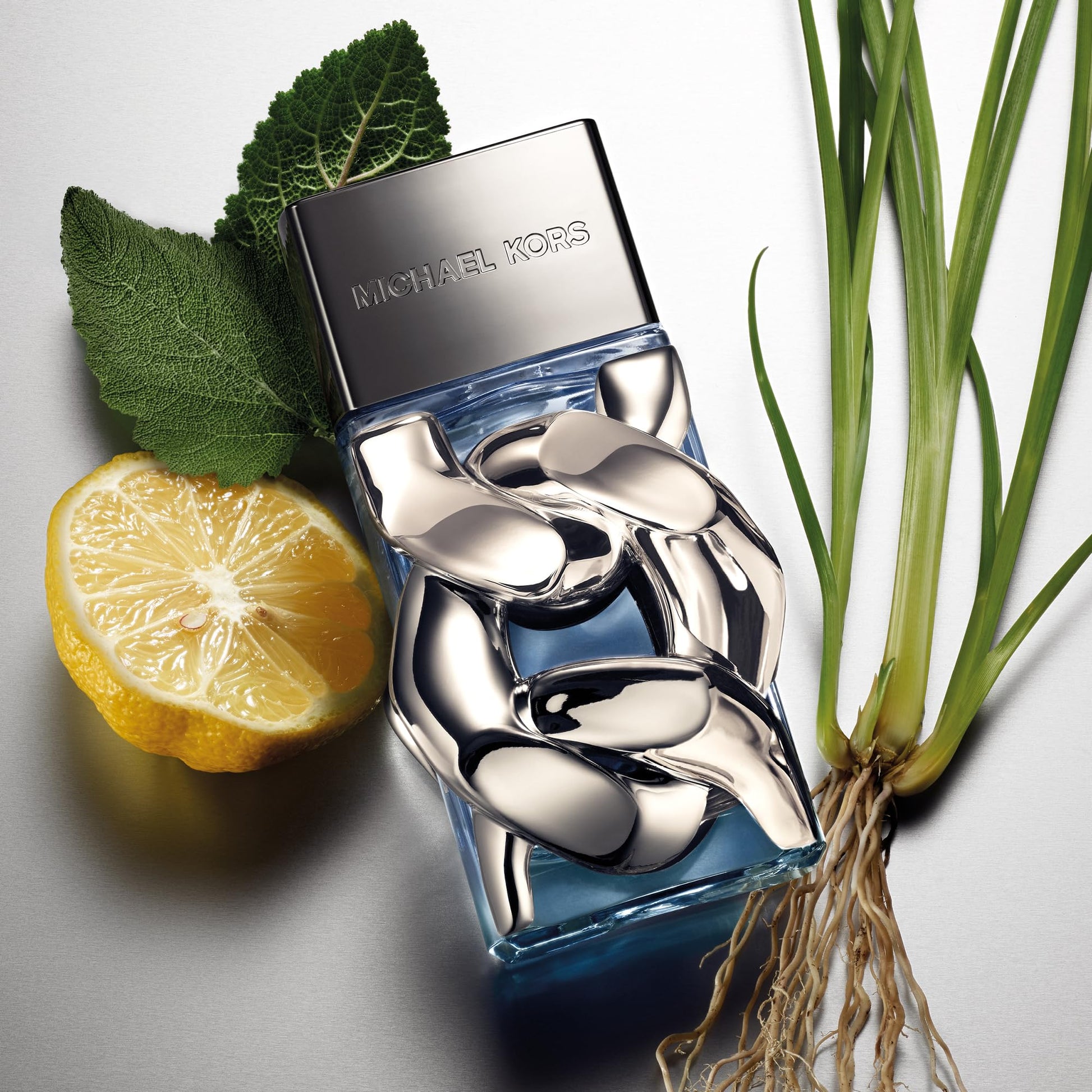 Blue Michael Kors perfume bottle with a lemon and plant on a light gray background
